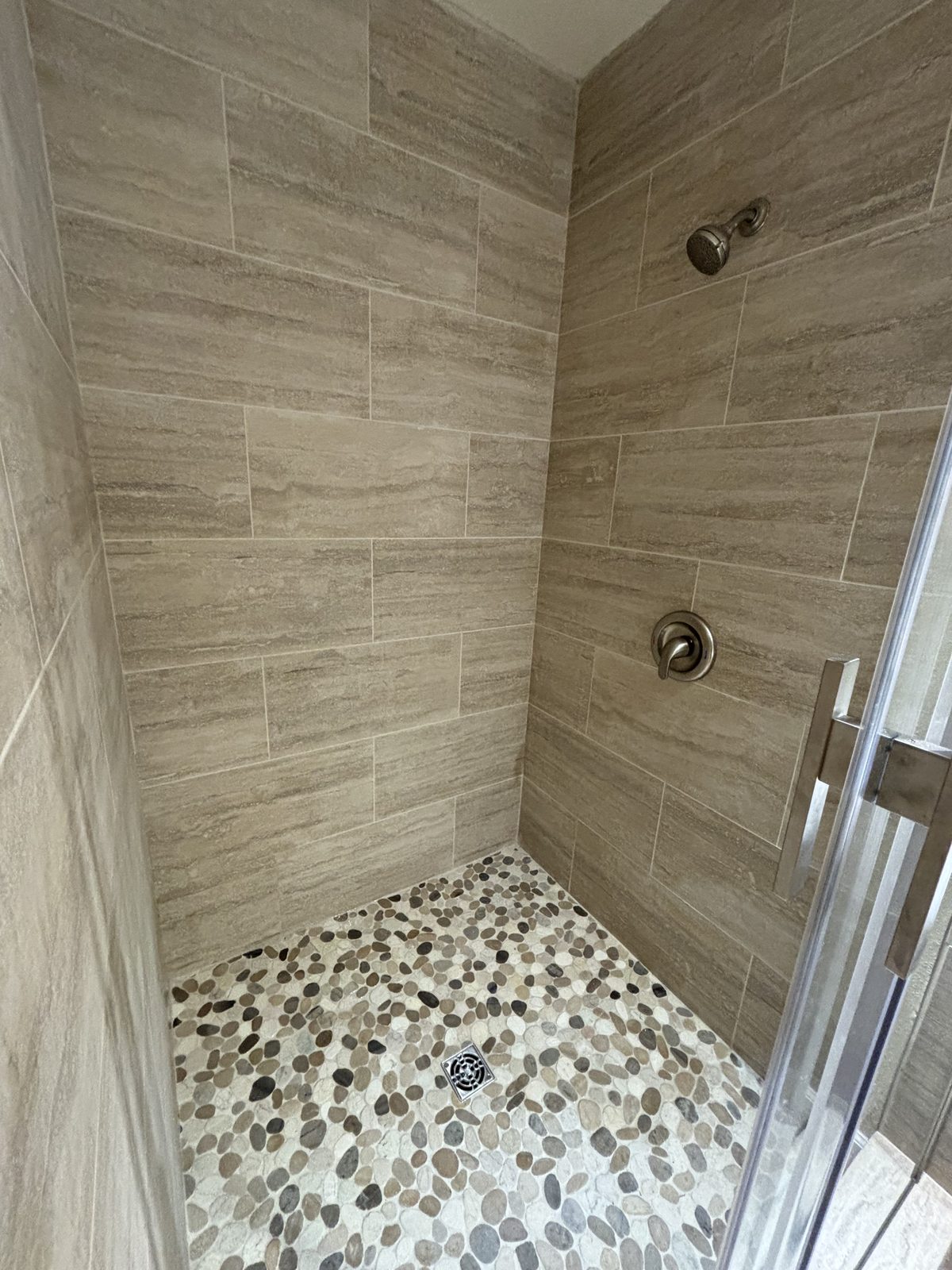 New tiled walk-in shower with pebble stone floor and sliding glass door